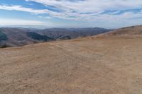 there is a bench on a hill near the mountains with a view of the hills in the back