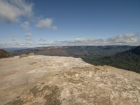 person with a backpack looking out over a rocky area at the mountains below them and an expansive river