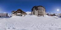 two buildings sitting at the bottom of a snow covered hillside with some buildings in front of them