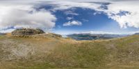 fisheye lens photograph of an animal standing on a mountain top with green grass and a river in the distance