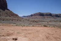 a dirt road through a desert plain with a mountain behind it and a clear blue sky in the background