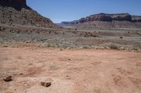 a dirt road through a desert plain with a mountain behind it and a clear blue sky in the background