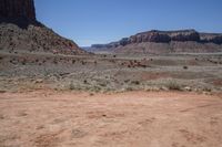 a dirt road through a desert plain with a mountain behind it and a clear blue sky in the background