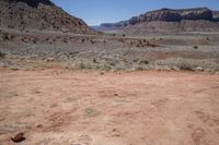 a dirt road through a desert plain with a mountain behind it and a clear blue sky in the background