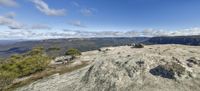 large boulders and rocks sit atop a rocky outcropping, with a clear blue sky in the distance