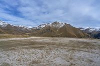 a view of the mountains from the top of a hill, looking toward a grassy hill area with tall, snow capped mountains