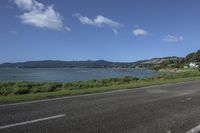 a motorcycle is parked by the edge of the road beside the water and hills in the background