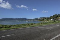 a motorcycle is parked by the edge of the road beside the water and hills in the background