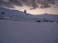 ski lift is sitting on the snow near the mountains at dusk overlooking a ski slope