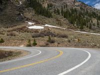 a mountain side with a road running next to the mountains, a bike parked in front of it and trees on one side