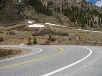 a mountain side with a road running next to the mountains, a bike parked in front of it and trees on one side