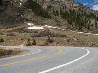 a mountain side with a road running next to the mountains, a bike parked in front of it and trees on one side