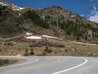 a mountain side with a road running next to the mountains, a bike parked in front of it and trees on one side