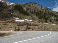 a mountain side with a road running next to the mountains, a bike parked in front of it and trees on one side