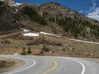 a mountain side with a road running next to the mountains, a bike parked in front of it and trees on one side