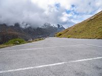 an empty parking lot in the mountains with some clouds moving across it and mountains behind