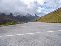 an empty parking lot in the mountains with some clouds moving across it and mountains behind