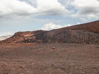 a dirt field that has a pile of rocks in the middle of it under a cloudy sky