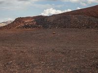 a dirt field that has a pile of rocks in the middle of it under a cloudy sky