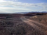 a dirt road stretches through a mountainous terrain area with rocky hills and mountains in the background