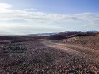 a dirt road stretches through a mountainous terrain area with rocky hills and mountains in the background