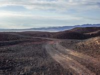 a dirt road stretches through a mountainous terrain area with rocky hills and mountains in the background