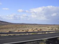 an asphalt road running through a desert area on a sunny day with blue sky and clouds in the background