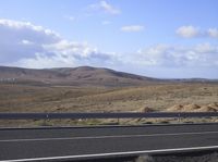 an asphalt road running through a desert area on a sunny day with blue sky and clouds in the background