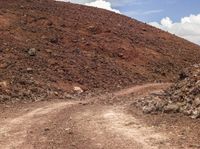 a dirt road winding down to a mountain of rocks, rocks and a cloudy blue sky