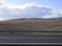 the view from the car window of a desert landscape with mountains, hills and a white building