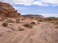 a dirt road surrounded by a big rock formation in the desert, with a blue sky overhead