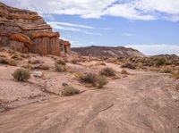 a dirt road surrounded by a big rock formation in the desert, with a blue sky overhead