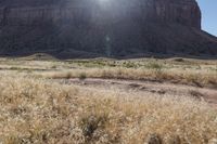 brown grass and dry ground in a mountainous area with the sun shining over a large rock