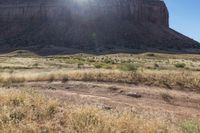 brown grass and dry ground in a mountainous area with the sun shining over a large rock