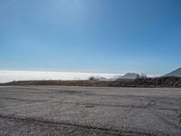 the sun shines brightly above some mountains and clouds on an empty tarmac with pavement