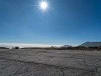 the sun shines brightly above some mountains and clouds on an empty tarmac with pavement