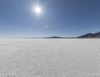 a white field with lots of sand under a sun and clouds in the background a mountain