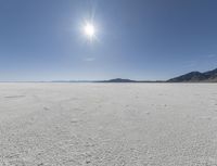 a white field with lots of sand under a sun and clouds in the background a mountain