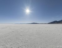 a white field with lots of sand under a sun and clouds in the background a mountain