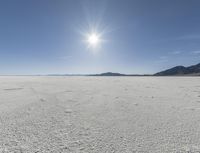 a white field with lots of sand under a sun and clouds in the background a mountain