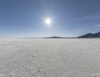 a white field with lots of sand under a sun and clouds in the background a mountain