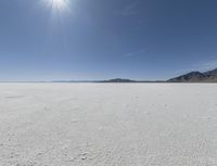 a white field with lots of sand under a sun and clouds in the background a mountain