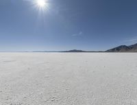 a white field with lots of sand under a sun and clouds in the background a mountain