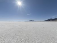 a white field with lots of sand under a sun and clouds in the background a mountain