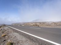 a road near the mountain side in the foggy sun day, and on the opposite bank are hills