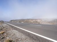 a road near the mountain side in the foggy sun day, and on the opposite bank are hills