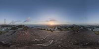 a sun setting behind the summit of a mountaintop overlooking a valley with buildings in the distance