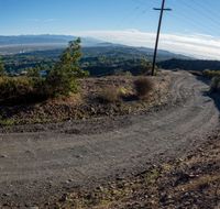 a dirt road leading to a mountain peak with many power lines on the side and hills in the background