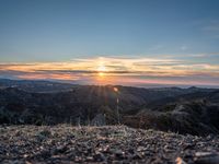 a lone motorcycle parked on top of a mountain with the sun setting over mountains in the background