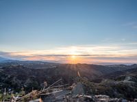 a lone motorcycle parked on top of a mountain with the sun setting over mountains in the background